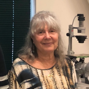 woman with shoulder-length gray hair standing in front of a microscope