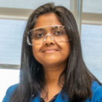 Photo of researcher Aindrila Mukhopadhyay wearing a lab coat and safety goggles