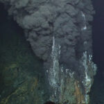 A photo taken in the deep sea. Black clouds billow out of hydrothermal vents.