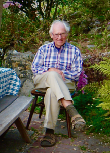 Photo of Ken Sauer sitting outside among green ferns and trees.