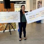 Anne Villacastin is pictured holding two large checks she received for winning first place and people's choice at the Berkeley Lab Research SLAM