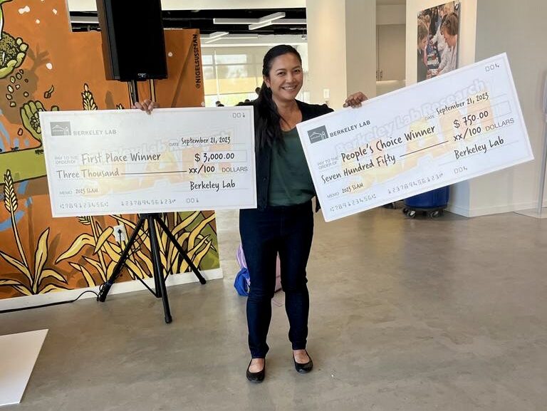 Anne Villacastin is pictured holding two large checks she received for winning first place and people's choice at the Berkeley Lab Research SLAM