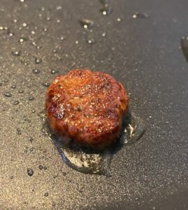 A red burger-like patty being cooked in a grey pan.