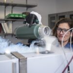 Female scientist smiles while pouring liquid nitrogen from a canister to the Fourier-Transform Infrared Spectroscopy (FTIR) device.