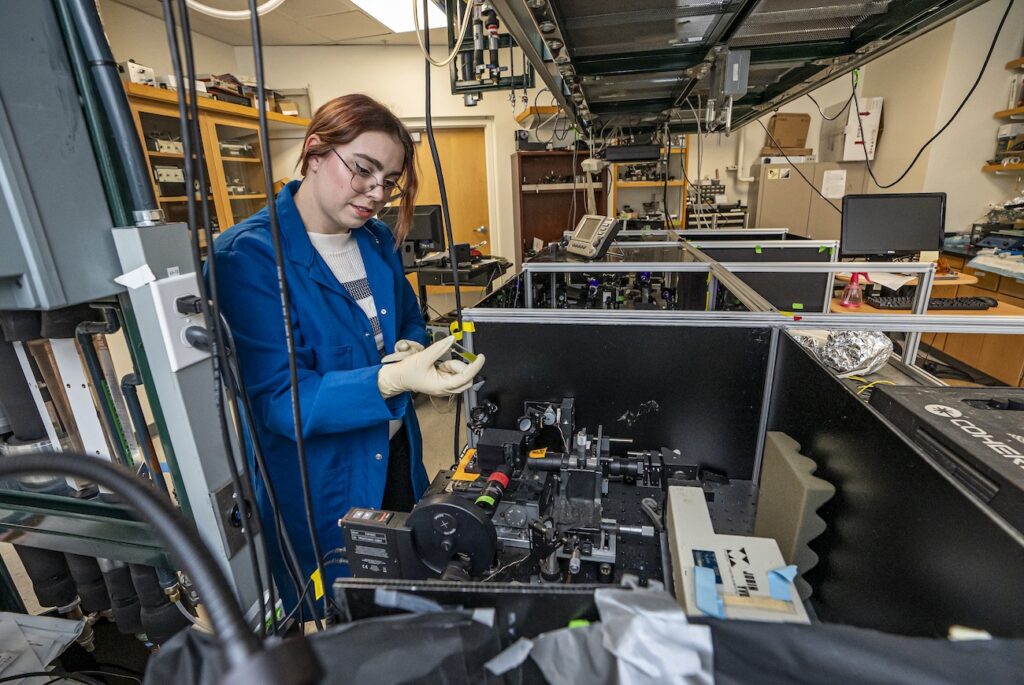 Graduate student researcher handles green algae samples in the lab while wearing gloves.