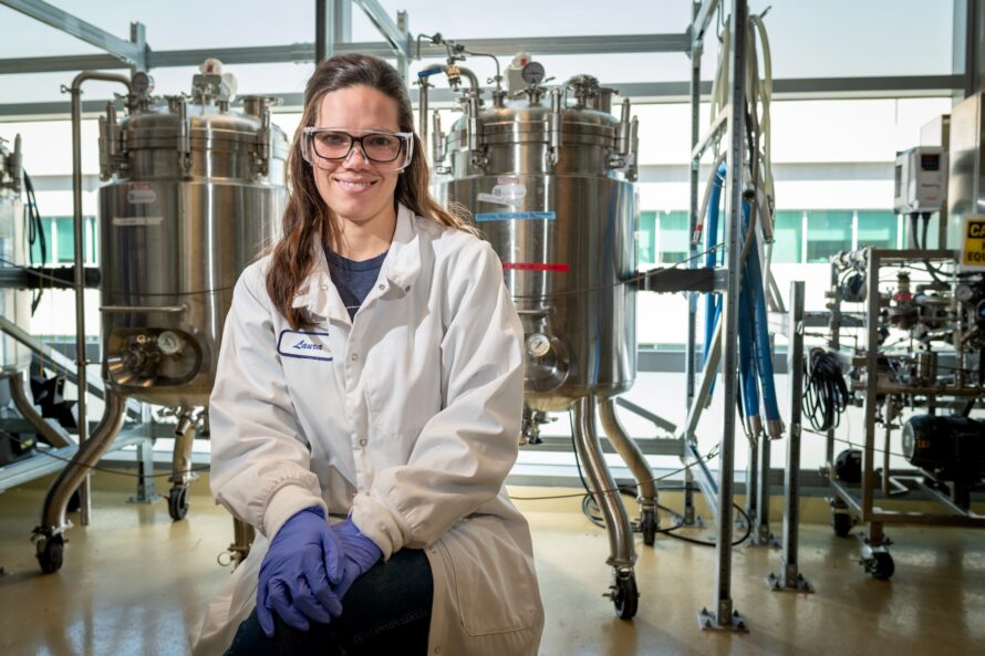 Portrait of a researcher photographed in front of industrial-sized fermentation reactors.