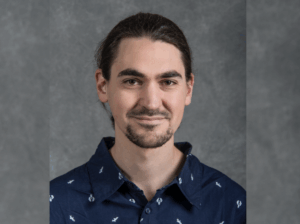Bearded man in dark blue print shirt against a gray background
