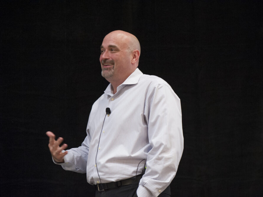 Blake Simmons, a bald man with a grey goatee and wearing a light grey dress shirt, gives a presentation.