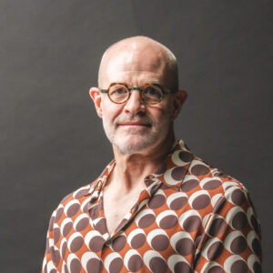 Jay Keasling, a bald man with a grey beard, wearing brown framed glasses and an orange shirt with white and brown circles