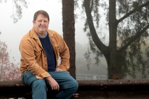 Photo of a person sitting comfortably in the foreground against a foggy, forested backdrop.
