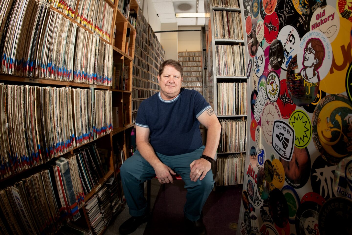 Photograph of a person sitting comfortably amid an extensive record collection.