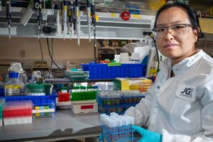 Research Scientist Hualan Liu holds tests tubes and poses by some pipetting equipment at the lab bench.