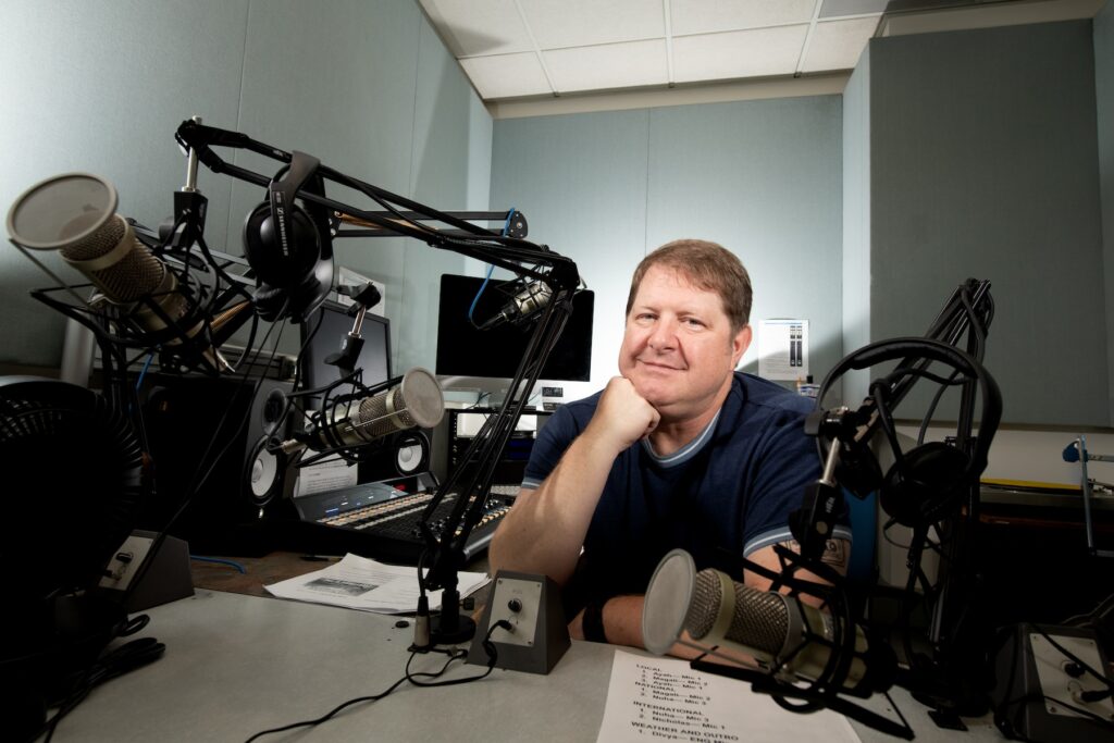 Person sits with their chin on their hand behind a microphone in a small room.