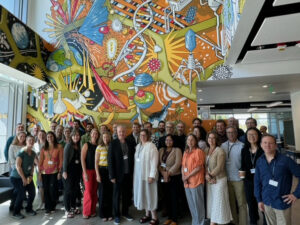 A group of people stands in front of the colorful scientific-themed wall mural with DNA strands and molecular imagery at the IGB.