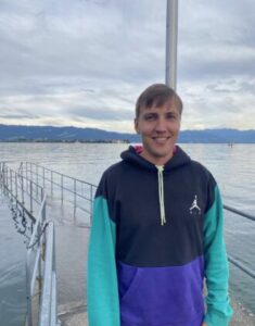 Graduate student Christian Tanner poses by a body of water, with green island in the background.