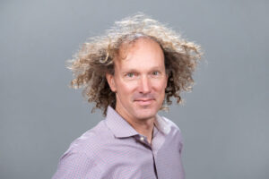 headshot of male scientist with curly blonde hair wearing a purple shirt
