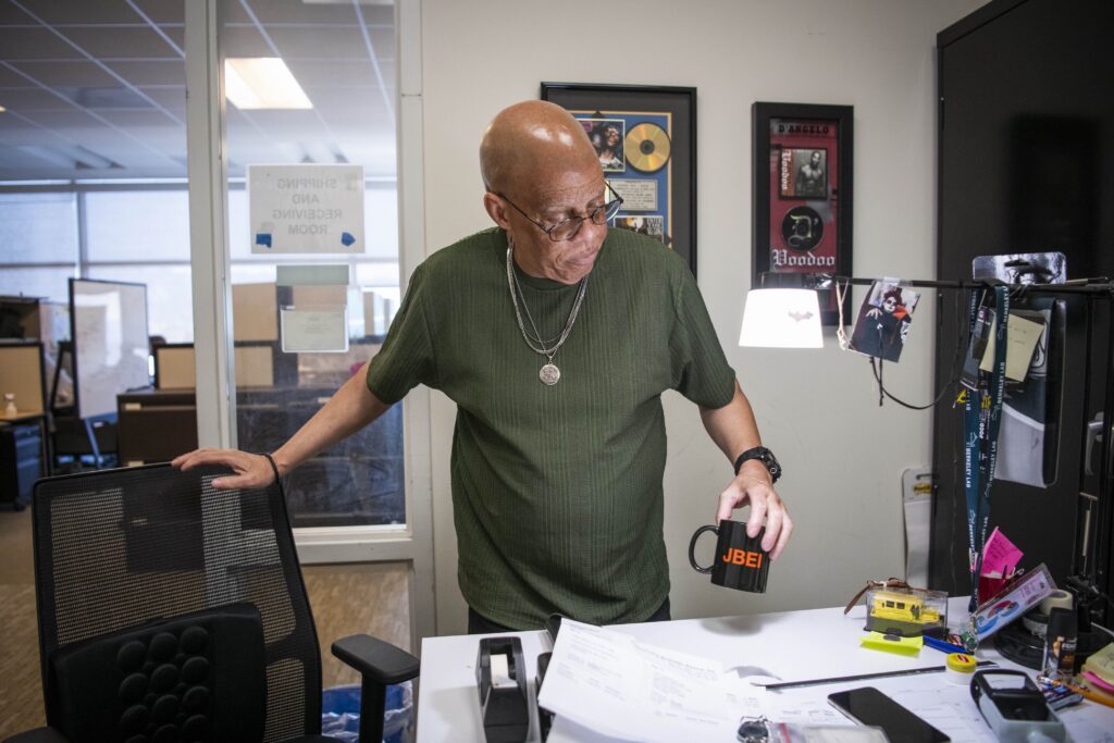 A person in an office holding a "JBEI" mug with paperwork on the desk.