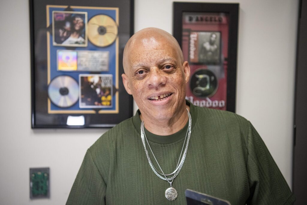 A person in a green shirt standing in front of two frames that hold music albums.
