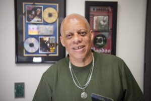 A person in a green shirt standing in front of two frames that hold music albums.